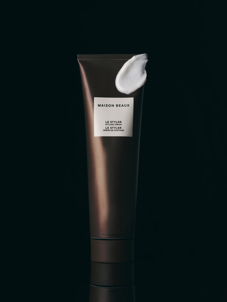 Le Styler 150 ML squeeze tube with a smear of the white styling cream on it, on a dark background.