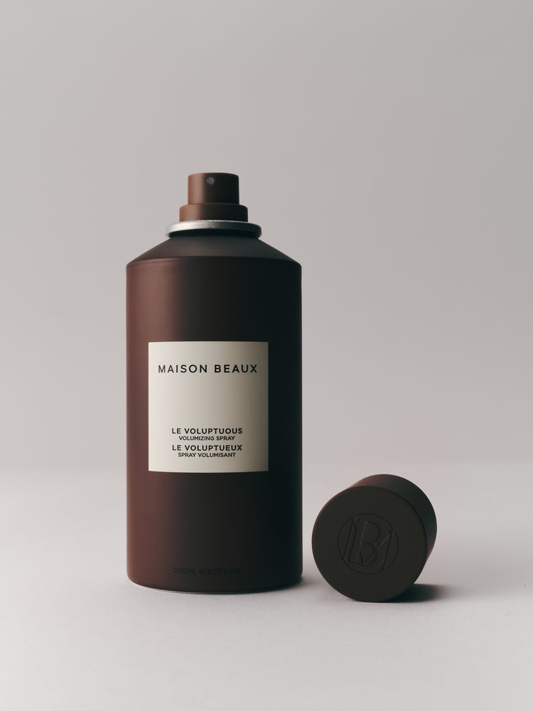 Le Voluptuous 250 ML spray bottle with cap off lying next to it, on a light backdrop.